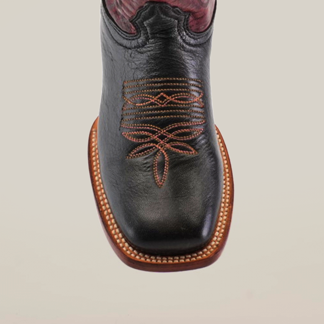 The Grecas Black boots feature a handcrafted design with intricate tan floral stitching on the square toe and a decorative brown sole, offering both style and uniqueness.