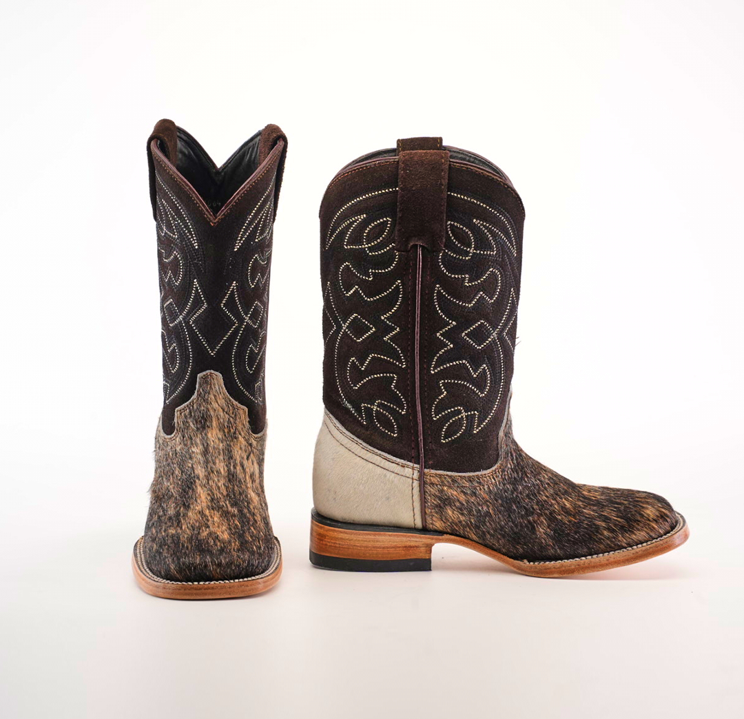 A pair of Cowhide Hair Fawn Square Toe boots features cowhide hair texture on the lower part, intricate white stitching on the dark brown upper; one boot is upright, and its sideways counterpart displays a square toe design, wooden heel, and back.