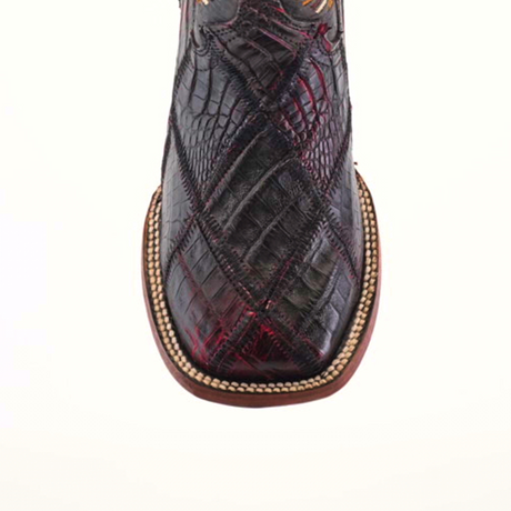 The Exotic American Alligator Patchwork Black Cherry Square Toe is a cowboy boot featuring rich brown and black cherry crocodile texture, visible from above. It has a square toe, detailed edge stitching like patchwork, and a sole with light decorative trim on plain white.