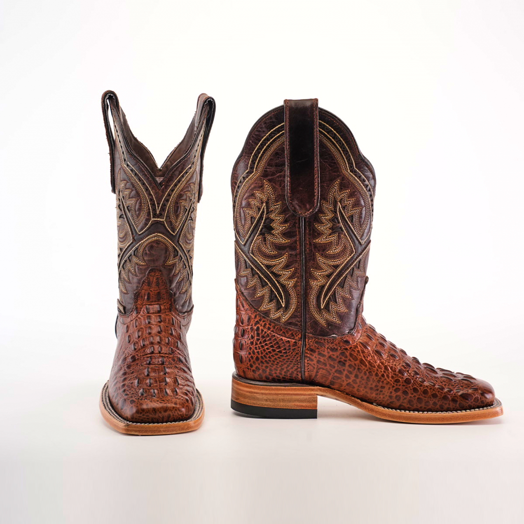 Two luxury cowboy boots crafted from textured brown leather with intricate stitching are shown against a white background. One features more embossing, while both have pull straps, wooden heels, and the elegant Caiman Hornback Print Chocolate Square Toe design.