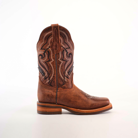 The Fresno Shedron Cowboy Boot features a detailed stitched design on the shaft and stands against a plain white background. With a rodeo toe, rounded design, and slip-resistant sole, it combines style and functionality with its wooden heel.