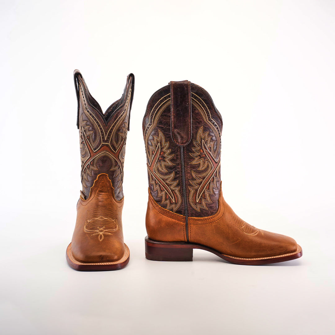 A pair of Cater Honey Square Toe boots, crafted from premium leather with detailed brown and tan stitching, is displayed on a white background. One boot stands while the other tilts, showcasing the superior craftsmanship and intricate embroidery around the shaft.