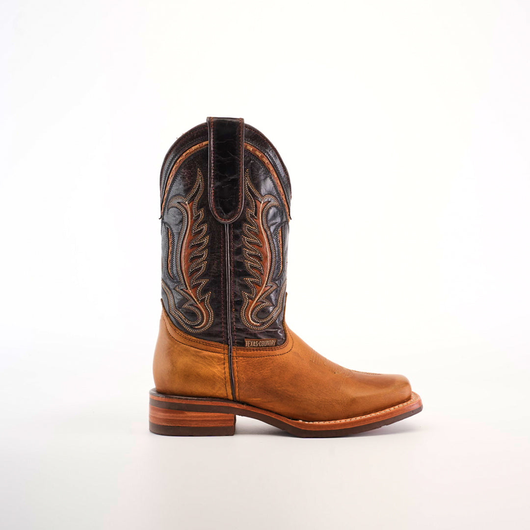 A single Cater Honey Slip Resistant Sole Rodeo Toe boot is showcased against a white background, highlighting its intricate brown stitching and dark leather accents. Crafted from premium leather, it features a wooden heel, detailed embroidery, and a slip-resistant sole for added stability.