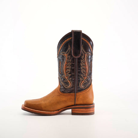 The Cater Honey Slip Resistant Sole Rodeo Toe boot features a brown cowboy design with decorative patterns on the dark leather shaft, a Rodeo toe, and a stacked heel. Made from premium leather, it includes a slip-resistant sole and pull strap, showcased against a white background.