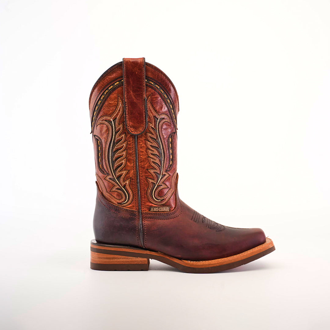 The Azkar Moka cowboy boot showcases intricate stitching on its shaft, has a medium heel, and features a light, slip-resistant wooden sole with a smooth finish. Its rodeo toe design adds flair against a plain white backdrop.