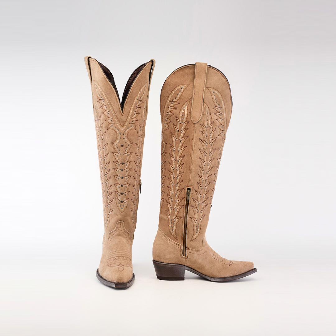 Presenting the Madona Sand Suede boots: a pair of Tall Shaft Snip Toe boots featuring intricate embroidery and side zippers. One boot stands upright, while the other is angled, revealing both front and side views.