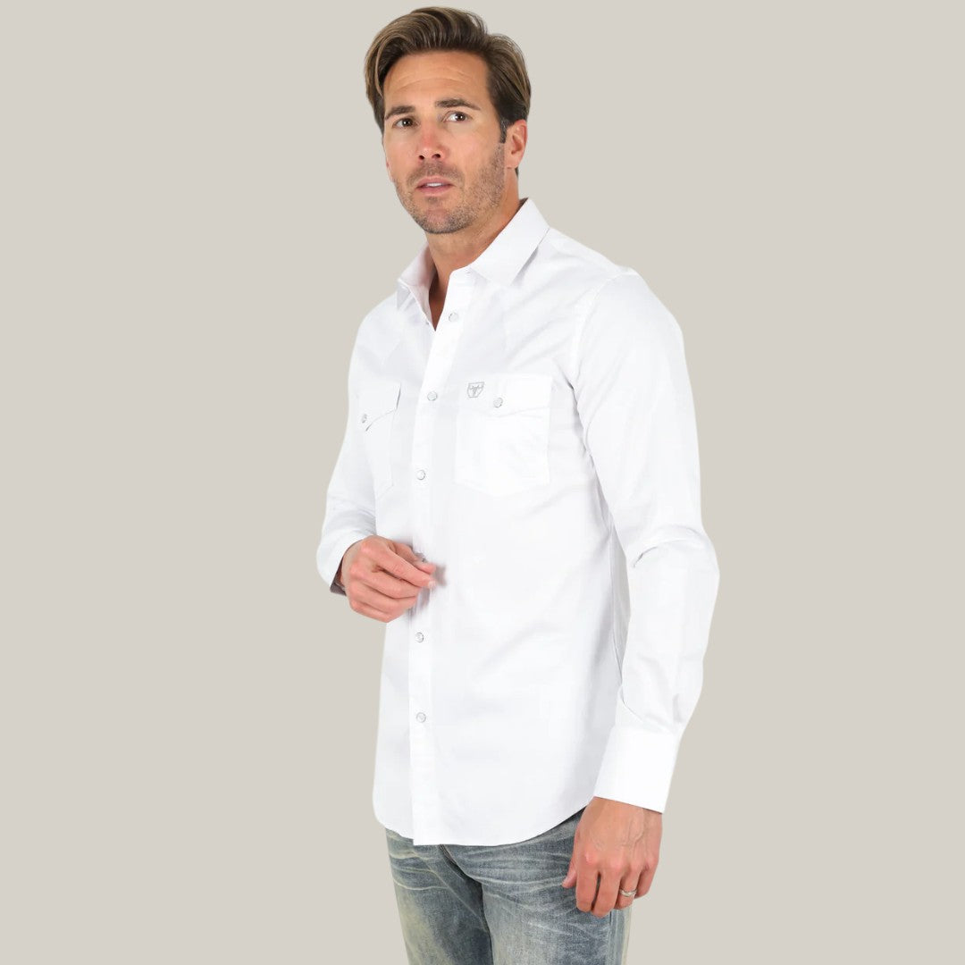 A man in a Men’s Single Pocket Logo Modern Fit Stretch Dress Shirt - White - CTL9259 and jeans stands against a gray background, gazing at the camera with a neutral expression. Crafted from breathable fabric, this premium shirt offers comfort and an effortlessly stylish look.