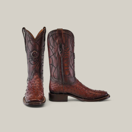 A pair of CU677 Flame Brown Ostrich cowboy boots features stunning laser and embroidery details, with one boot upright showing its square toe and the other angled to display the side and front against a light gray background.