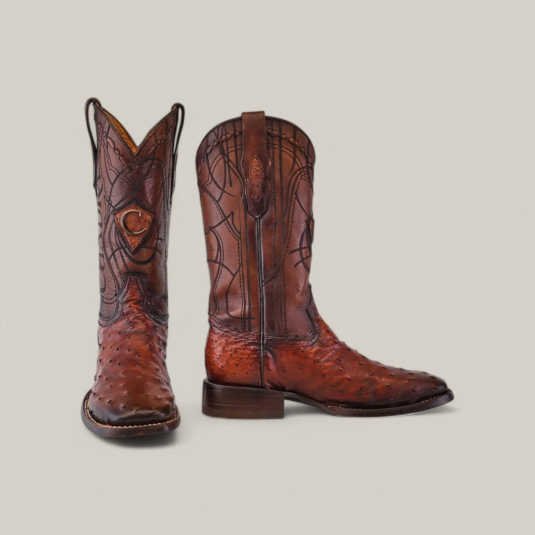 The Moroni Chestnut Ostrich Laser & Embroidery - Square Toe - CU457 cowboy boots, featured on a plain gray background, highlight their square toe design. One boot is upright while the other lies on its side, showcasing intricate detailing along with the heel and sole.