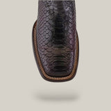 Close-up of a black snakeskin leather boot with a square toe, detailed scale texture, and brown stitched welt, inspired by the chic Lisboa Cherry Python Embroidery & Laser & Woven - Square Toe - CU746. The background is light gray.