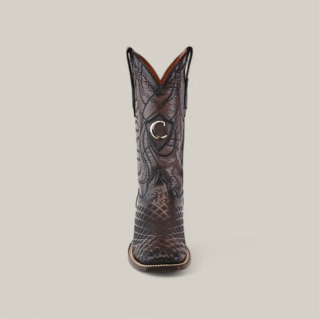 A single brown cowboy boot with intricate stitching and a shiny, textured pattern is featured. It has a stylish crescent-shaped emblem near the top, similar to Cuadras Over Black Laser & Embroidery & Woven Square Toe - CU676, set against a plain beige background.