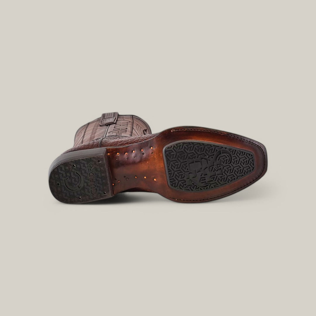 The image shows the bottom view of a Brown Moreletii Laser & Embroidery CU700 cowboy boot, crafted from alligator leather, on a light gray background. The sole displays distinct patterns with a circular logo and intricate designs, and the heel is slightly elevated.