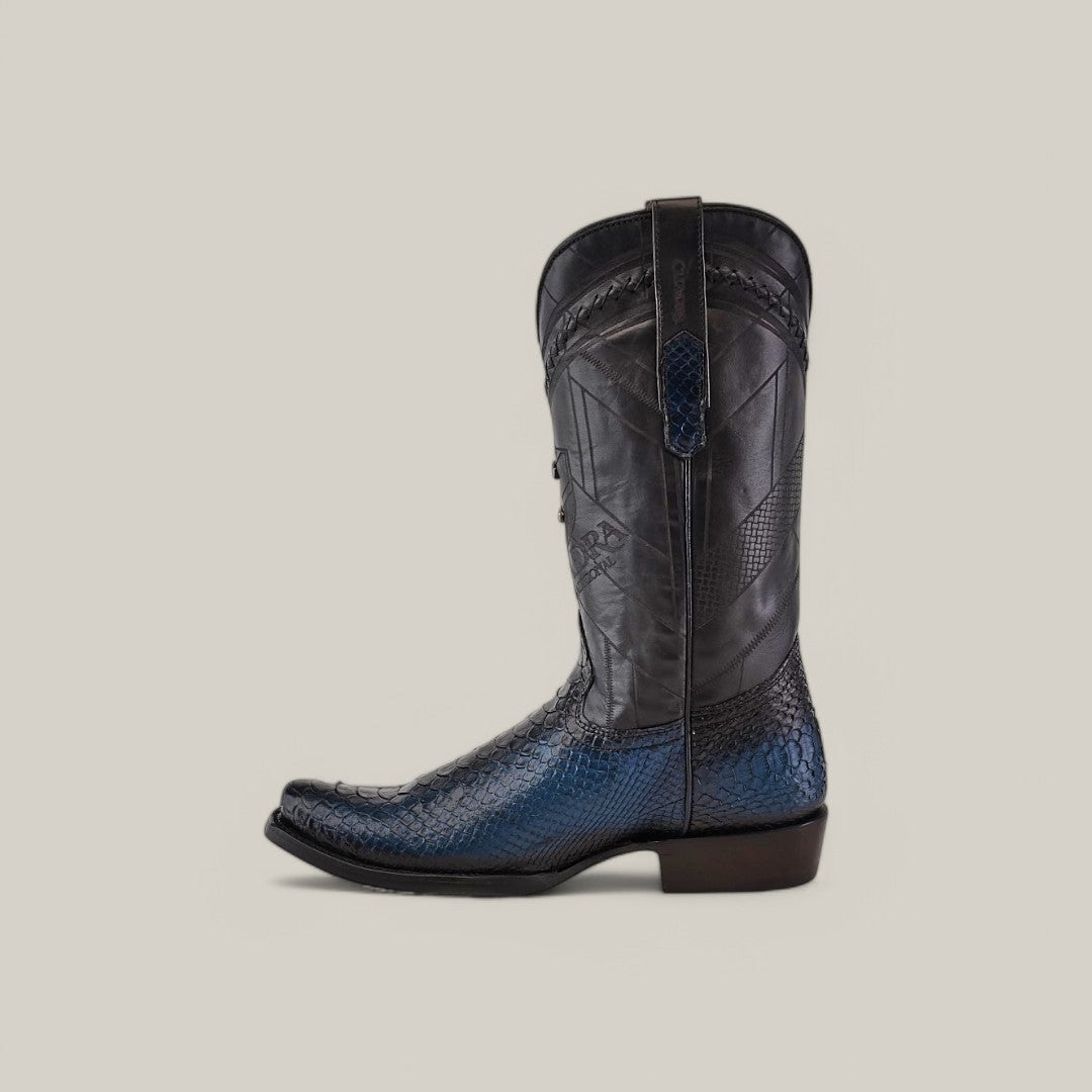 The Lisboa Blue Python Laser & Woven boot (CU736) by Cuadra has a narrow square toe, black shaft, dark blue textured python leather lower portion, intricate stitching on the upper part, and a low dark heel, shown in profile against a light gray background.