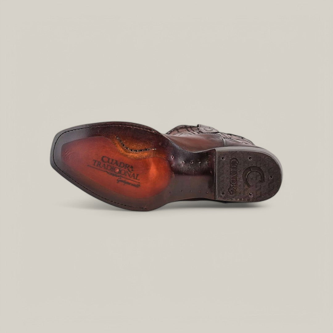 The image shows the underside of a Cuadra Over Chestnut Laser & Embroidery shoe with visible stitching. The sole features engraved text and designs prominently displaying CUADRA TRADICIONAL. Set against a plain, light background, it evokes their iconic Narrow Square Toe style (CU347).