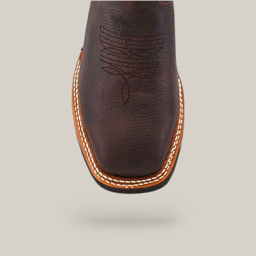 The Taurus Moka Soft Toe - E6189 is a brown leather masterpiece featuring intricate toe stitching and a square design. Its double-row white stitch along the soles edge enhances durability, while the light gray background showcases its rugged elegance.