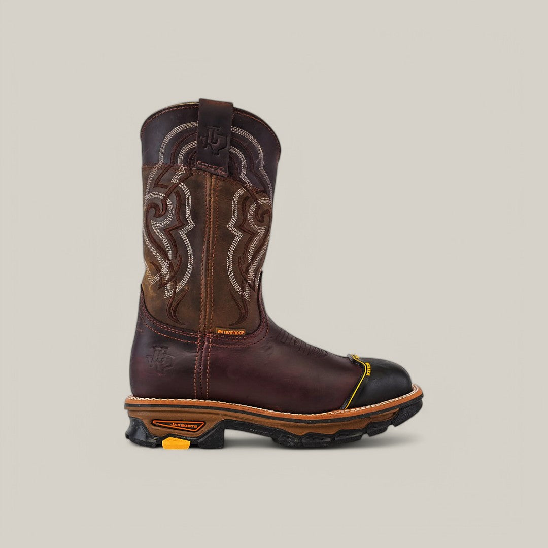 The Amazonas Chocolate Composite Toe - E6258 is a brown leather cowboy boot with intricate shaft stitching, a rounded black toe cap, and a durable rubber sole. It has a pull strap, a small heel logo, and is ideal for Texas Country Work Boots fans, set against a plain light gray background.