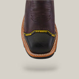 A close-up of the Amazonas Chocolate Composite Toe - E6258, a dark brown leather boot with intricate stitching and a black toe cap labeled Jar Boots and Western World in yellow. It features a light brown sole with white stitching, showcasing rugged craftsmanship.