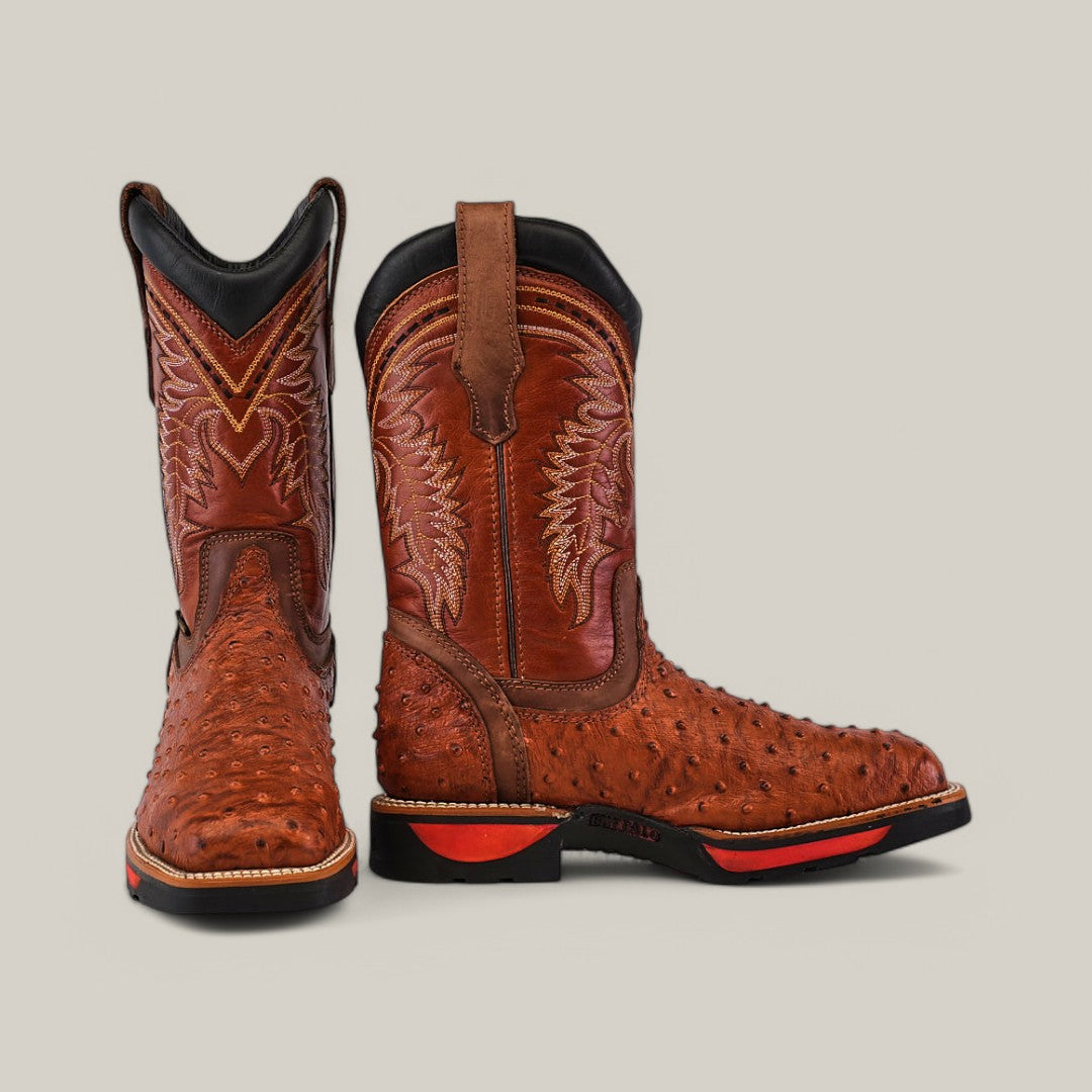 The Texas Country work boots, Ostrich Print Cogñac Soft Toe - E6022, are crafted from durable ostrich leather with detailed stitching. These waterproof brown boots have a black sole with red accents and brown pull straps, all highlighted against a light gray background.