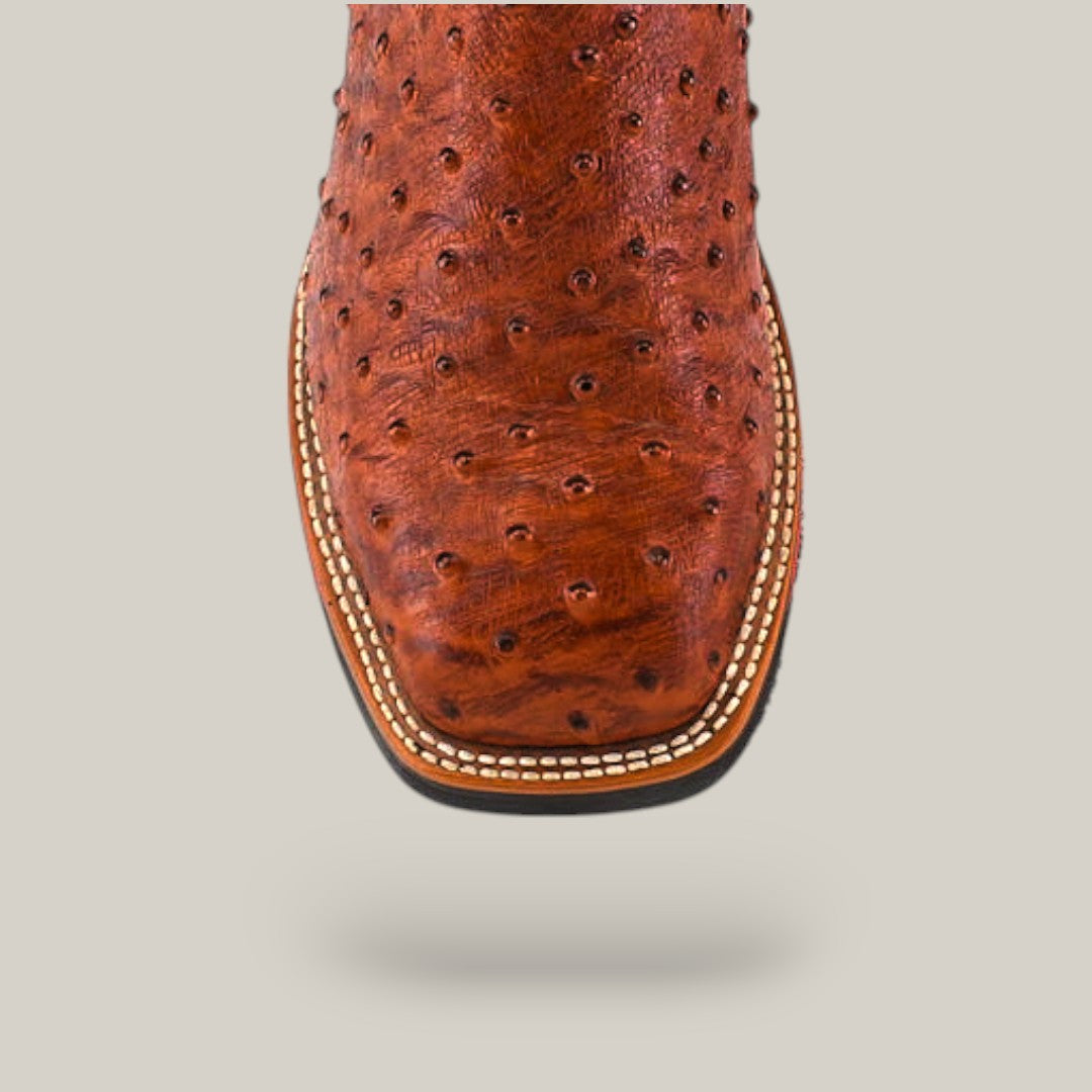 A close-up of the Ostrich Print Cogñac Composite Toe - E6022 showcases its square toe and textured, ostrich-like brown leather. Detailed stitching around the sole enhances its durability. The boot stands prominently against a plain background, embodying Texas Country Work Boots craftsmanship.