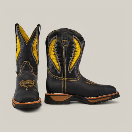 The Rhino Black Composite Toe - E6087 is a pair of black cowboy boots featuring brown soles, intricate yellow stitching, and embroidery on the shafts, reflecting the durability and comfort of Texas Country Work Boots. One boot faces forward while the other shows a side view.