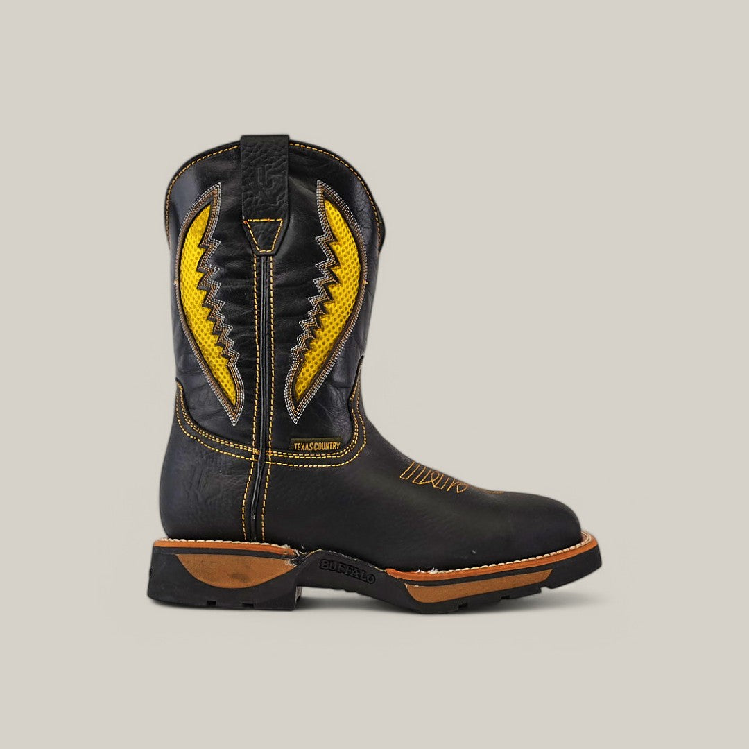 The Rhino Black Soft Toe - E6087 boot, featuring yellow stitching, a leather pull tab, and a brown sole for durability and comfort, exemplifies rugged elegance against a beige background.