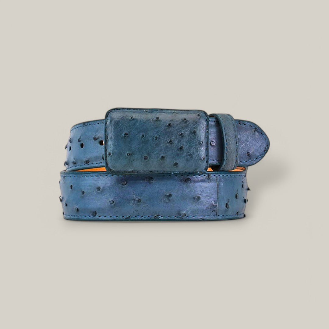 The Exotic Full Quilt Ostrich - Blue Jean Belt, made of luxurious blue leather with a dotted texture and a matching rectangular buckle, is neatly coiled against a light grey background.