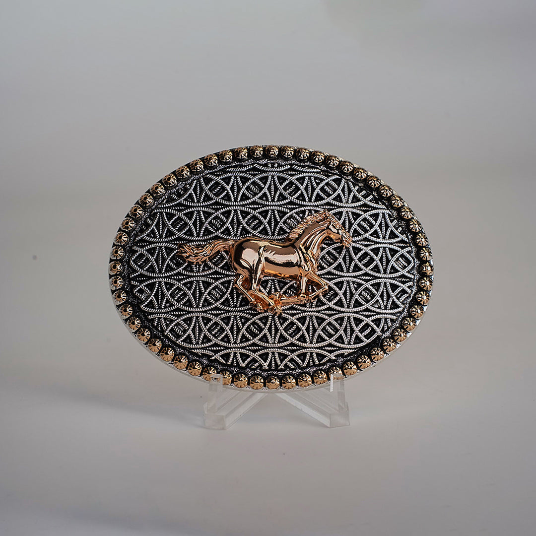 The Racing Horse Buckle is an oval belt accessory featuring a gold horse design at its center amidst intricate geometric patterns, reminiscent of classic Texas buckles. It includes small gold accents along the edge and is displayed on a clear stand against a neutral background.