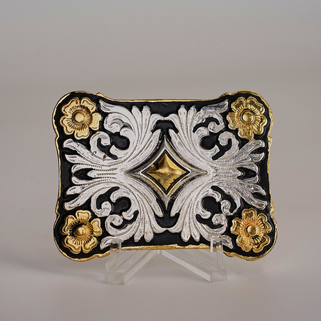 The Floral Diamond Gold Buckle is an ornate plaque with intricate western-style scrollwork, gold floral accents on a black background, and a central raised gold diamond shape, all showcased on a clear stand.