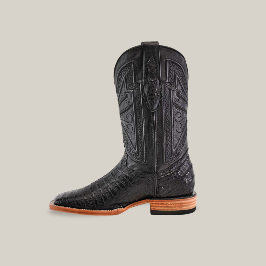 The Exotic Caiman Belly in black, perfect for Cowboy Connoisseurs, features intricate shaft stitching, a square toe, and a wooden stacked heel with a leather sole, elegantly displayed against a plain beige background.