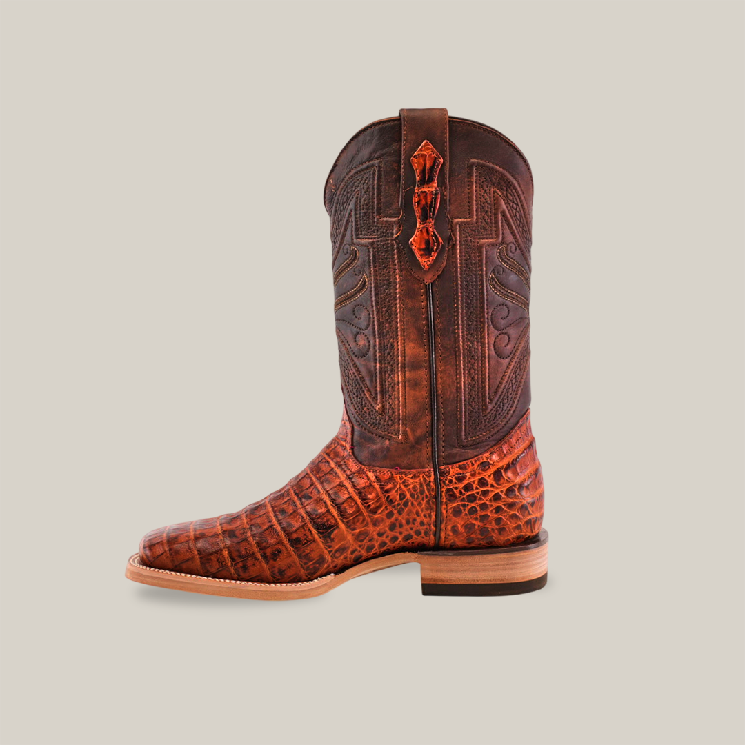 The Exotic Caiman Belly - Brandy - Square Toe boot features a brown upper with intricate stitching and an orange, caiman belly-textured lower portion. It boasts a classic wooden heel and functional pull straps on top.