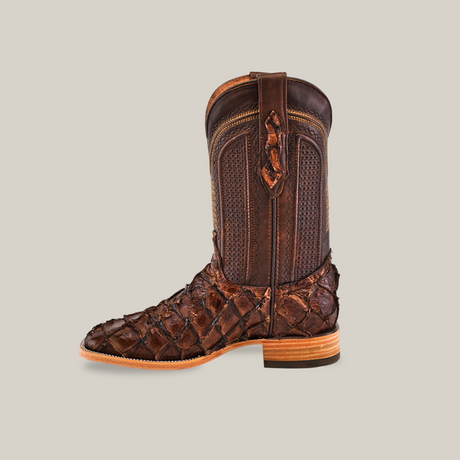 The Exotic Pirarucu Fish boot in brown, featuring a square toe, showcases a textured diamond-patterned foot, smooth upper shaft, light brown sole, and small heel that embodies Western fashion against a simple backdrop.