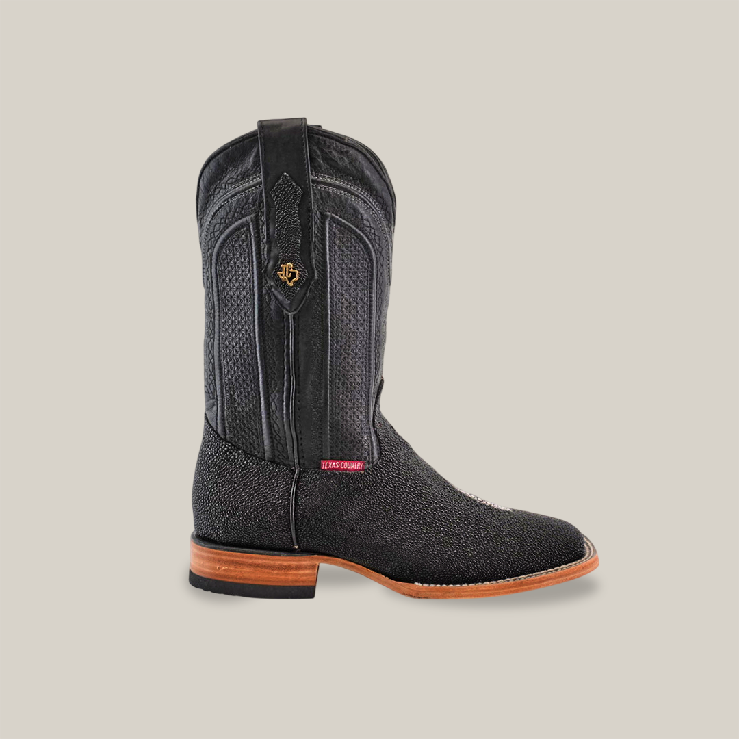 The Exotic Stingray - Black boot boasts a textured leather surface with a decorative emblem near the top, exuding Western luxury charm. Its square toe and brown wooden sole complement the exotic stingray finish, all set against a neutral background.