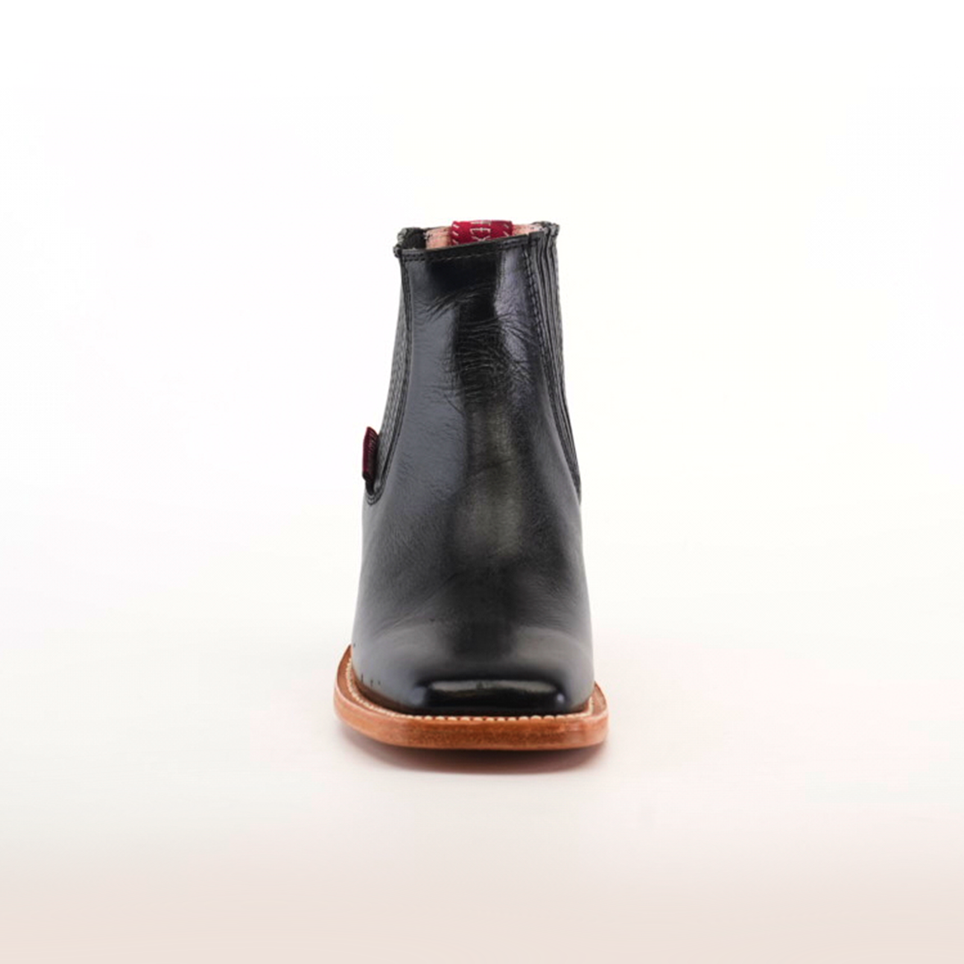 The Napa Black Square Toe Ankle Boot, with a smooth finish, brown sole, and slight heel, is elegantly showcased on a soft off-white background. Its sleek design makes it an essential piece for any fashion-forward wardrobe.