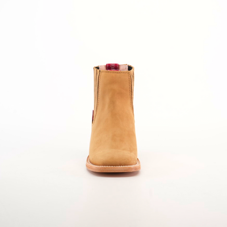 The Prime Suede Honey Square Toe is showcased against a white background. Featuring a tan suede hue, this ankle boot has a flat sole and square toe. A red plaid and beige pull tab adds contrast, embodying the Cowboy Fashion trend.