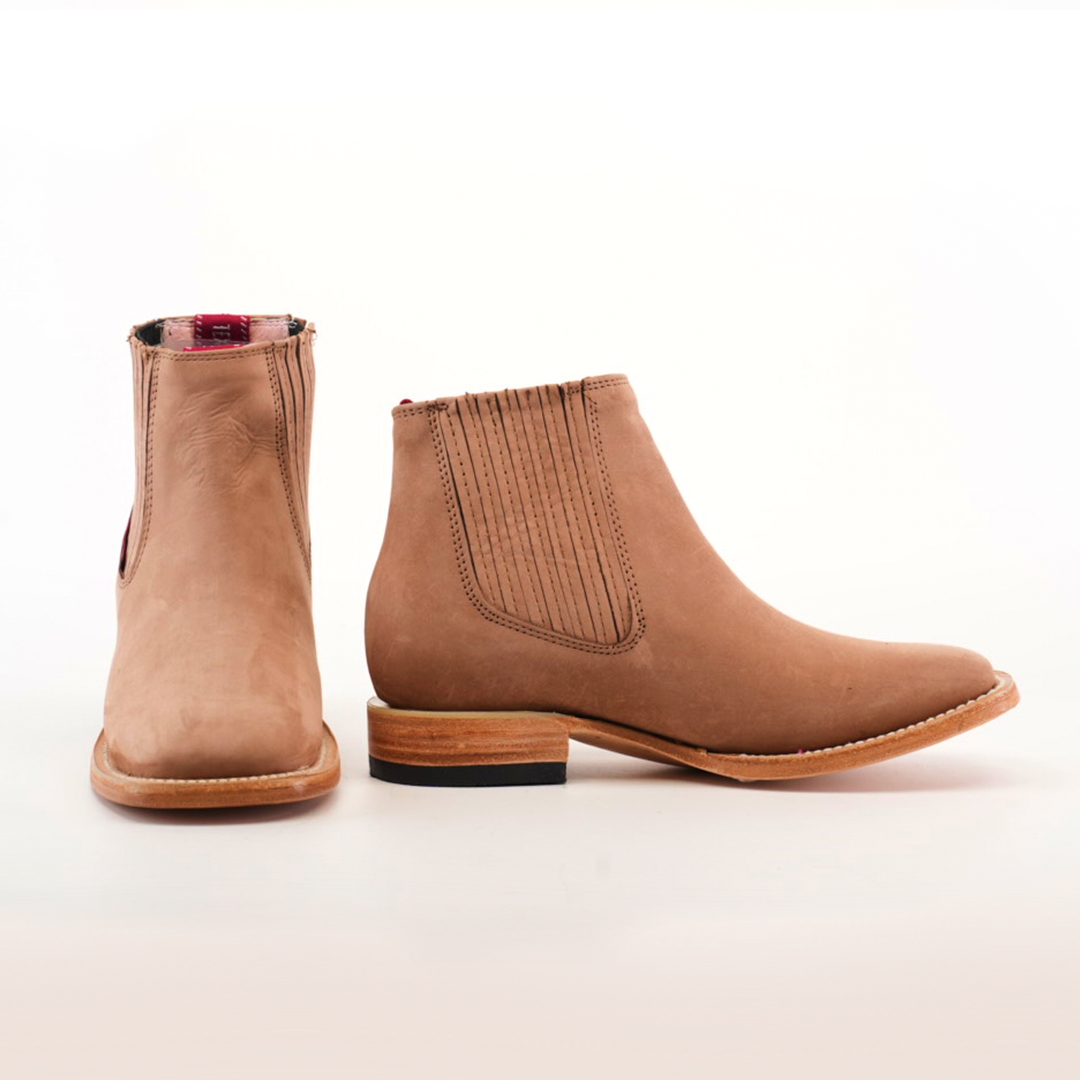 Displayed against a plain white background are the Prime Suede Sand Square Toe boots. The left boot is shown front-on and the right from the side, highlighting an elastic panel and wooden sole—ideal for any fashion-forward wardrobe.