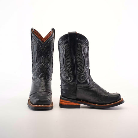 The Karoo Ostrich Half Cowhide Print Black Rodeo Toe boots feature a western aesthetic with intricate stitching and wooden soles. Displayed on a plain white background, one boot faces forward while the other is in profile, showcasing the detailed design.