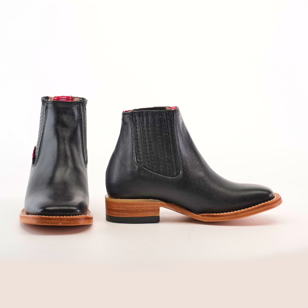 A pair of Napa Black Square Toe Chelsea boots, made from genuine leather with side elastic panels and contrasting tan soles, are displayed on a light background. One boot is positioned forward while the other shows a side view, emphasizing their luxurious craftsmanship.