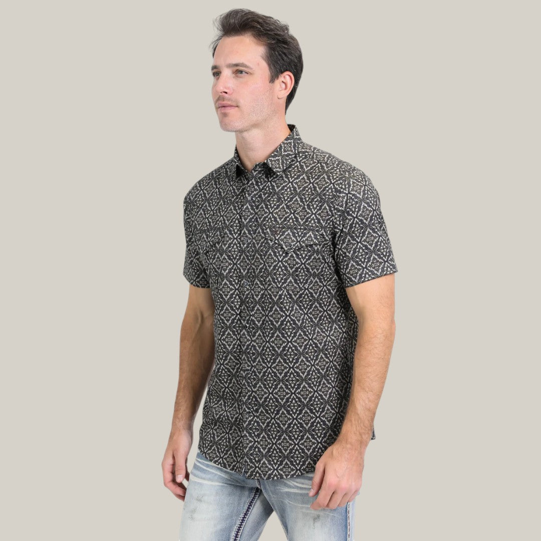 A man stands against a plain background wearing the Mens Performance Western Short Sleeve Aztec Print Black/Brown Shirt - PGW10635, paired with light blue jeans.