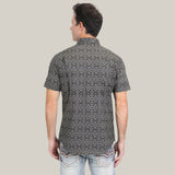 A man with short dark hair faces away wearing the Mens Performance Western Short Sleeve Aztec Print Black/Brown Shirt - PGW10635 paired with light blue jeans. The simple light grey background highlights his stylish choice.