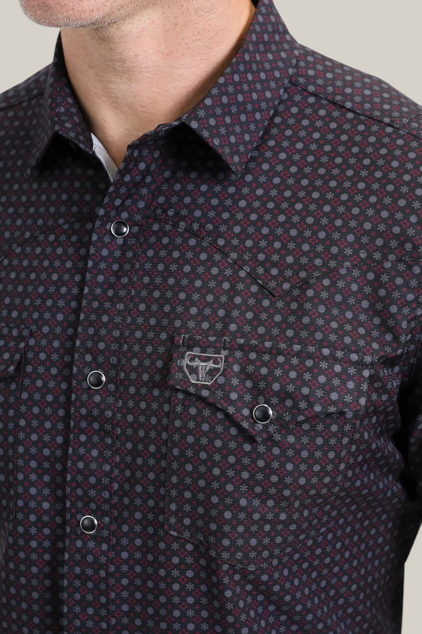 A person wearing the Mens Performance Western Short Sleeve Aztec Print Black Shirt (PGW10639) with geometric patterns and metal buttons, featuring a chest pocket with embroidered details. The person’s face is partially out of the frame.