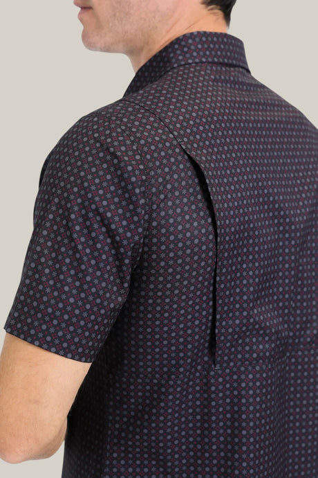 A person wears the Mens Performance Western Short Sleeve Aztec Print Black Shirt (PGW10639), showcasing its dark geometric Aztec design with an open back flap against a plain light gray background, where only their back and side profile are visible.