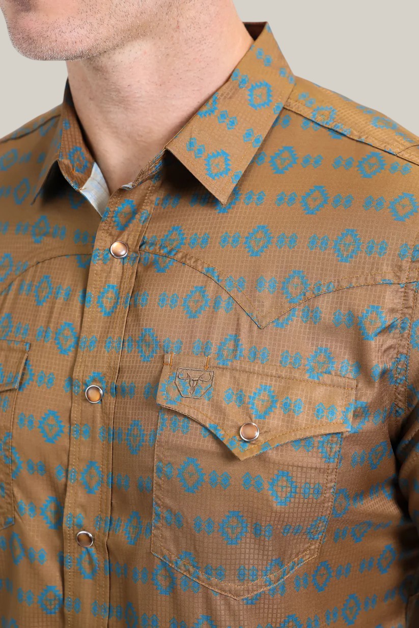 Close-up of someone wearing the Mens Performance Western Short Sleeve Aztec Print Camel Shirt - PGW10613. This mens shirt features lightweight, breathable fabric with blue geometric patterns, two chest pockets with button details, and an embroidered motif on one pocket against a neutral background.