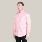 A person wears the Men’s Single Pocket Logo Modern Fit Stretch Dress Shirt in pink (CTL9826) with black pants, standing against a gray backdrop and glancing to the side.