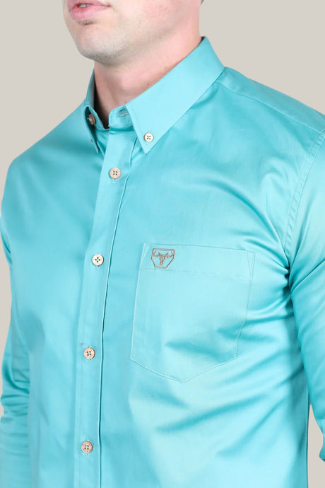 A person is dressed in the Men’s Single Pocket Logo Modern Fit Stretch Dress Shirt - Turquoise (CTL9829). Its made from stretch fabric with a button-down collar, wooden buttons, and features a small embroidered logo pocket. They are shown from shoulders to waist against a light gray background.