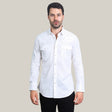 A dark-haired, bearded man wears the stylish Mens Western Modern Fit White Shirt (WPL10484), crafted from cotton and spandex. The shirt features snap buttons and two chest pockets, paired with black pants against a plain light gray background, as he looks directly at the camera.