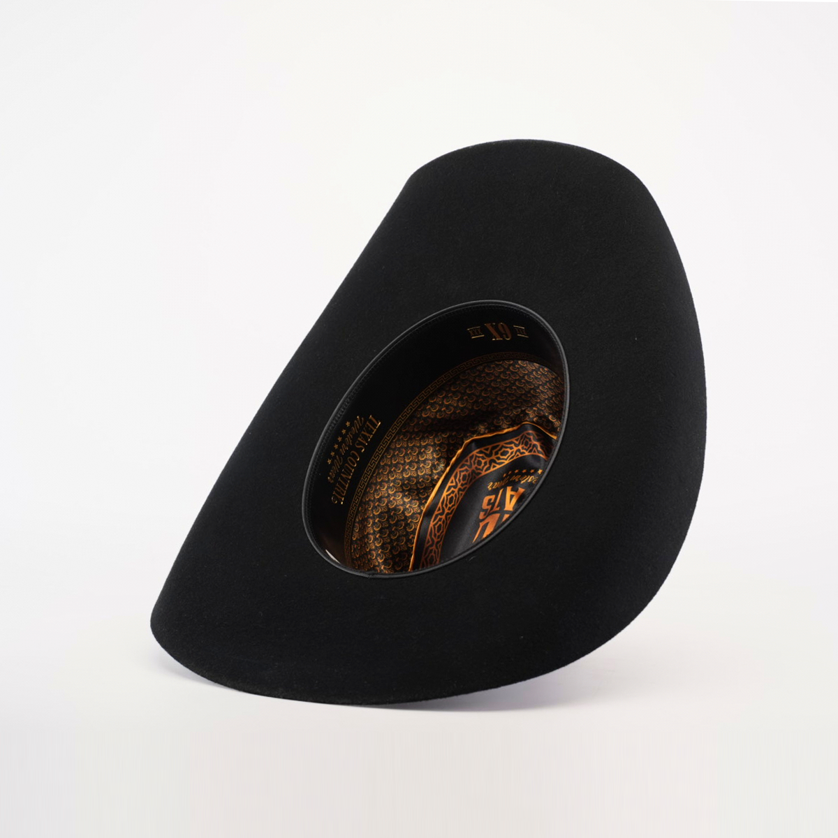 The 6X Chihuahua Black is a felt hat with a wide brim and angled crown, featuring an intricate pattern inside in gold and brown hues, lying on a pristine white surface.