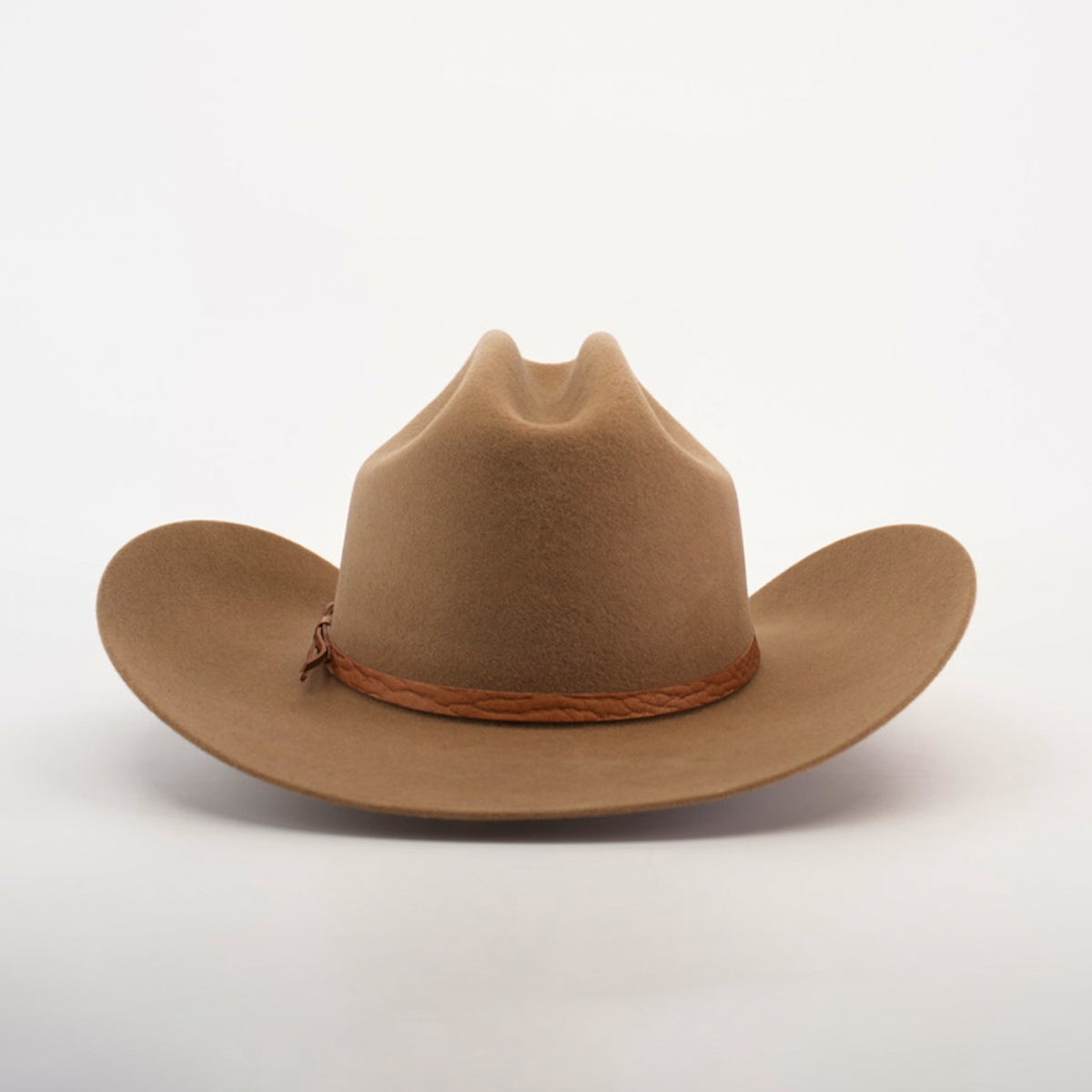 The 6X Country Fawn is a brown felt cowboy hat crafted from sheep wool, featuring a braided leather band. It rests on a plain white background, with a wide, slightly curled brim complementing its high, creased crown.