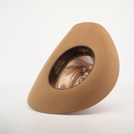 The 6X Country Fawn cowboy hat is shown upside down, revealing its intricate interior details. The brown felt hat boasts a patterned inner band with Resistol printed inside, all elegantly contrasted against a plain white background.