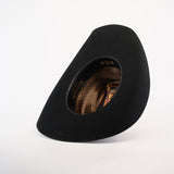 The 6X Bull Black hat, featuring an asymmetrical wide brim and a patterned brown interior, is set upright on a white background. Its unique shape exudes an artistic, modern vibe and captures the luxury essence of western wear.