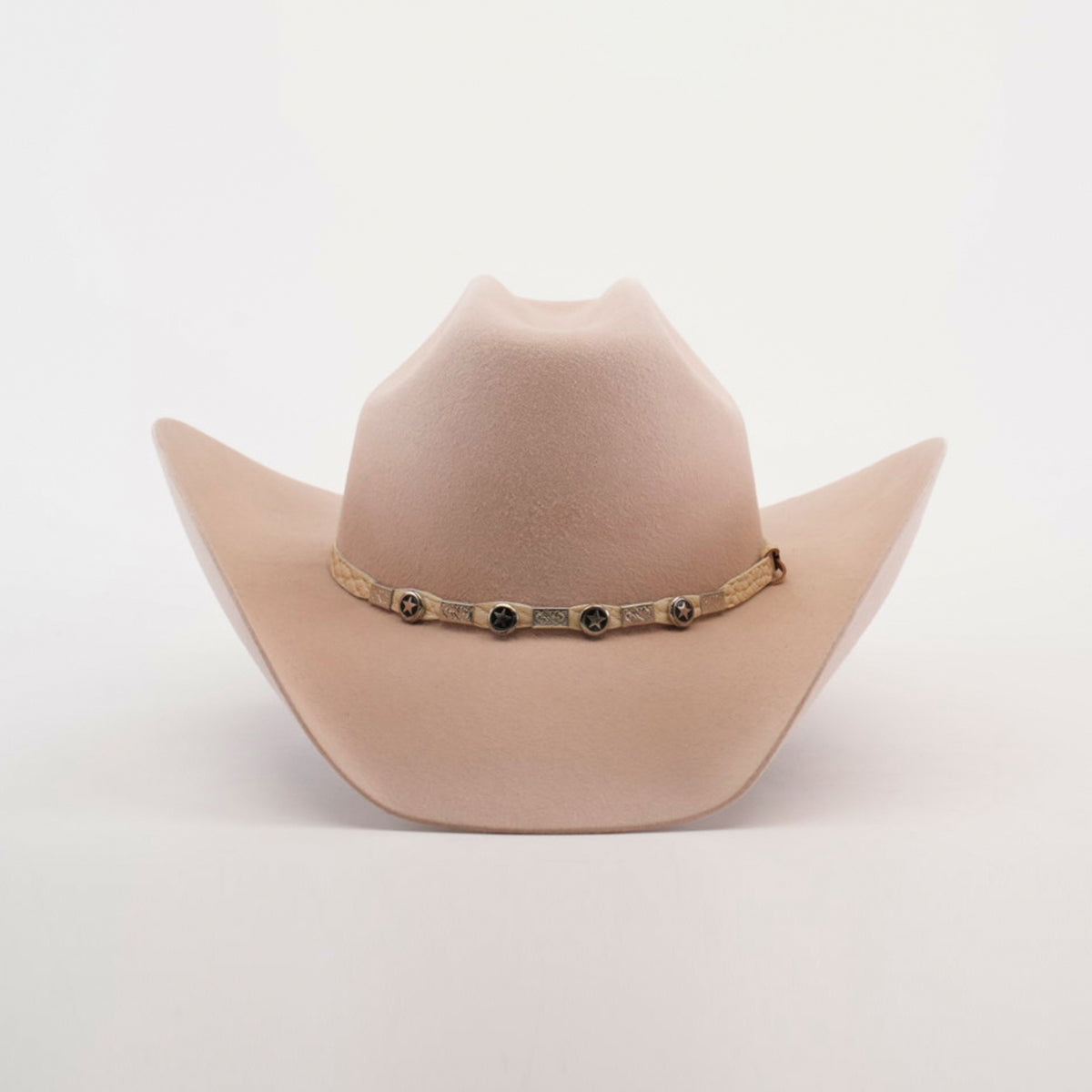 The 6X Bull Belly is a luxury western wear accessory featuring a light beige cowboy hat with a wide brim and adorned with round metal accents on the decorative band around the crowns base, all set against a plain white background.